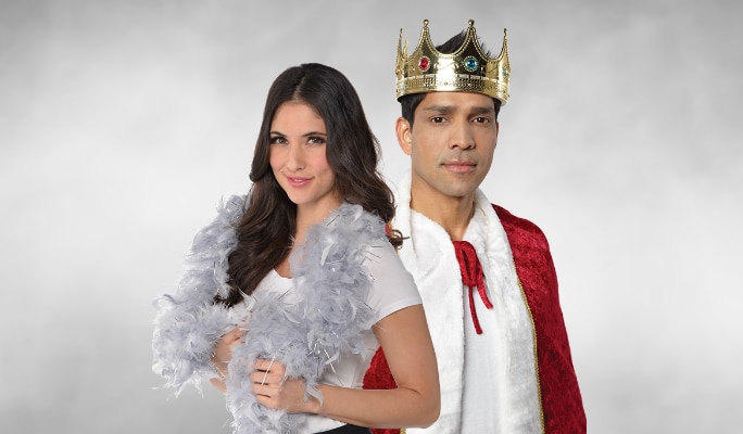 A woman wearing a grey feather boa and a man wearing a jeweled costume crown and cape.