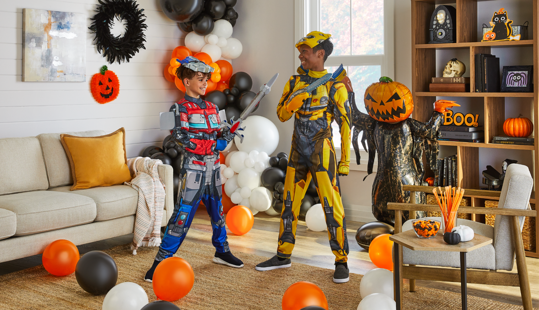 Deux enfants portant des costumes Transformers dans une pièce remplie de ballons et décorations d’Halloween.