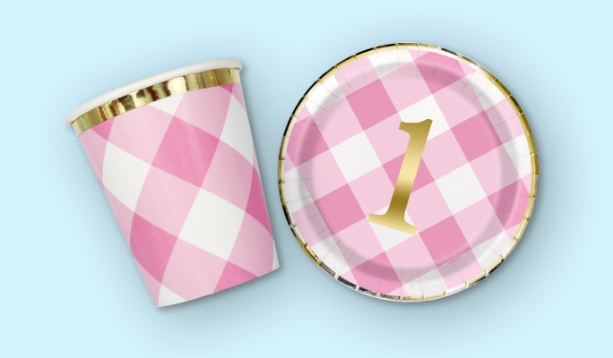 A pink gingham 1st birthday party paper plate and paper cup.