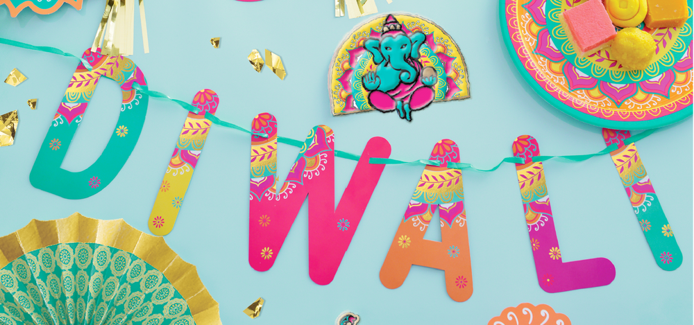 A mix of Diwali decorations including a multi-coloured Diwali banner, a foil embossed elephant window decoration, a green and gold paper fan and a multi-coloured round plate with rangoli design.