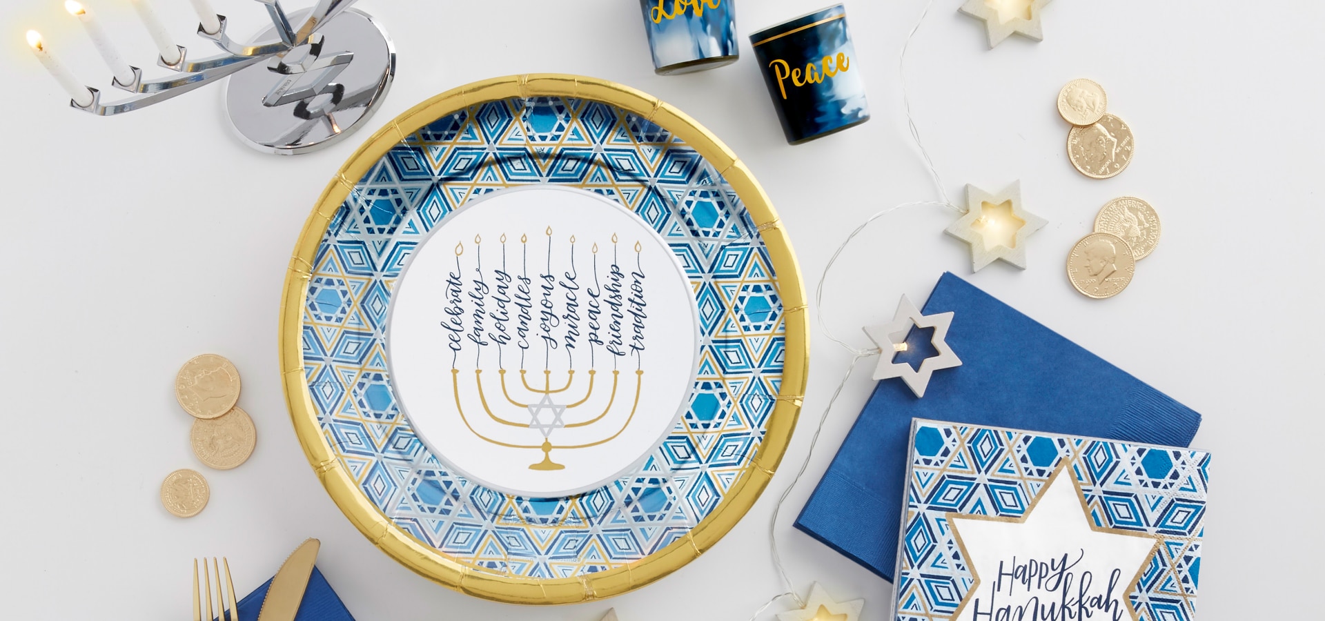 Une table agrémentée d'un chemin de table de la Hanoukka bleu marine, d'une ménorah de couleur argent et d'autres services de vaisselle et accessoires de couleur bleue, argent et or.