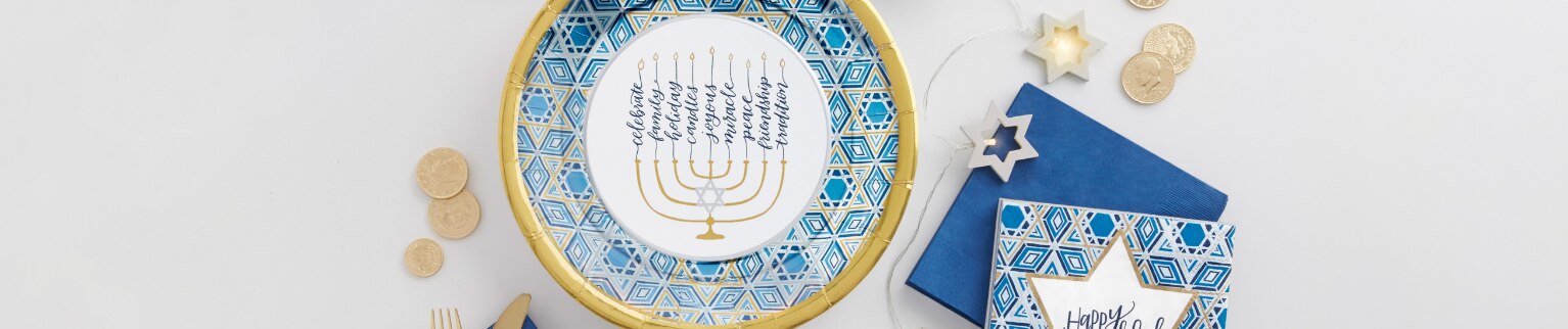 A menorah, plate, napkins, cups, cutlery, coins and star string lights on a white table.