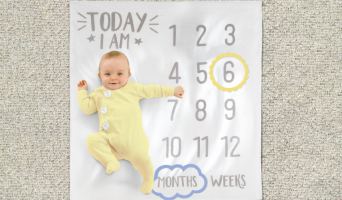 Un bébé sur une couverture blanche et grise pour prendre des photos d’étapes importantes.