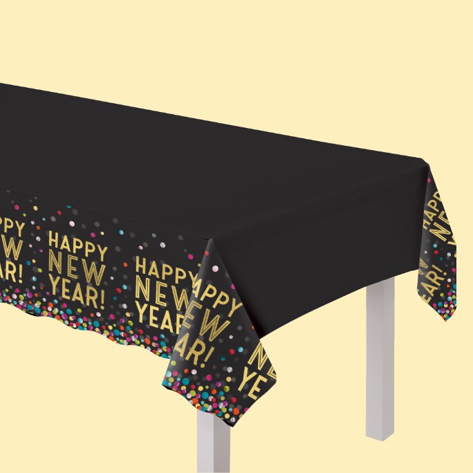 A table covered with a black tablecloth with 'Happy New Year!" repeated on it in gold font.