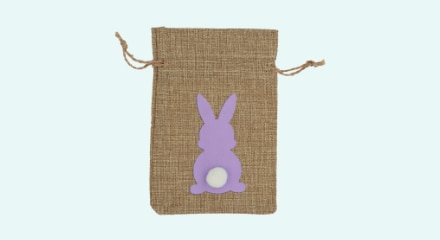 A brown burlap gift bag with a purple bunny and a plush white tail. 