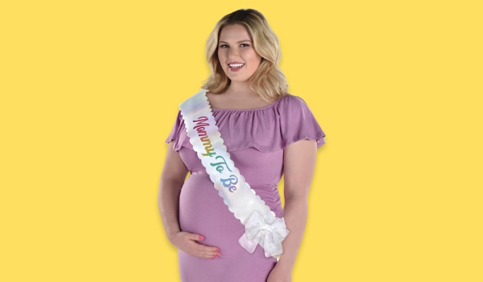 A pregnant woman wearing a white sash that reads "Mommy To Be"