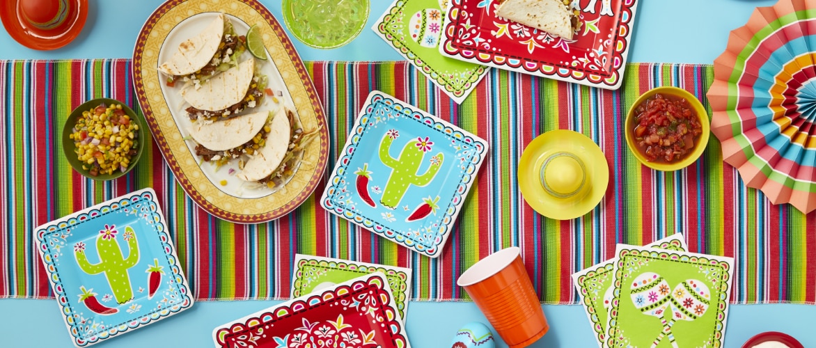 A table decorated with fiesta-themed napkins, tableware, tacos, guacamole and salsa.