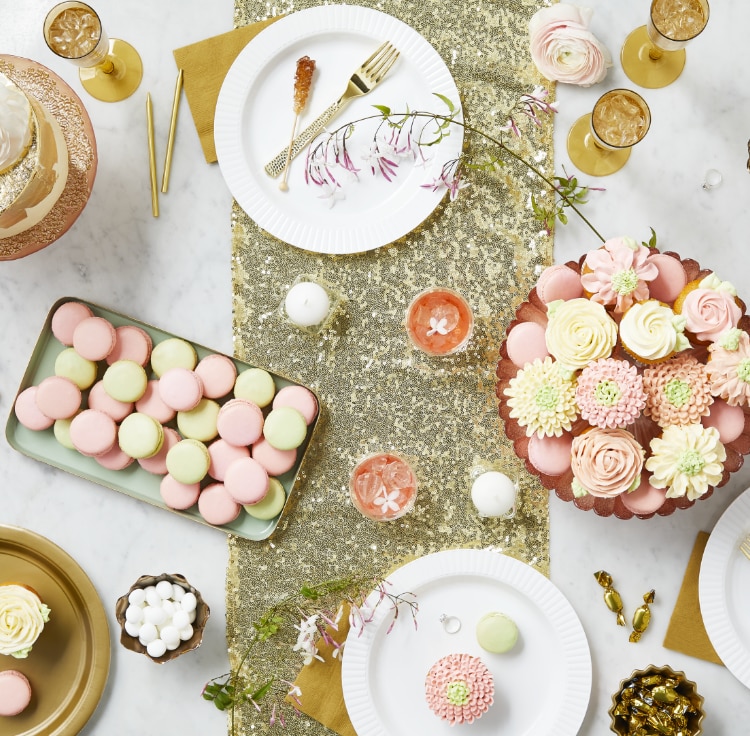A dessert table styled with white, pink and gold decor, plates, cookies and cupcakes.