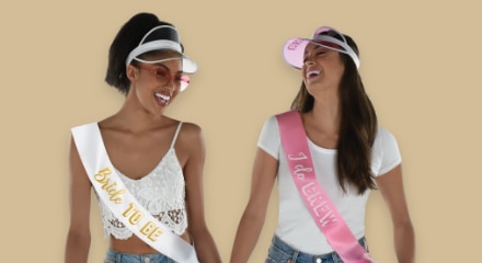 Two women wearing bachelorette-themed visors and sashes.