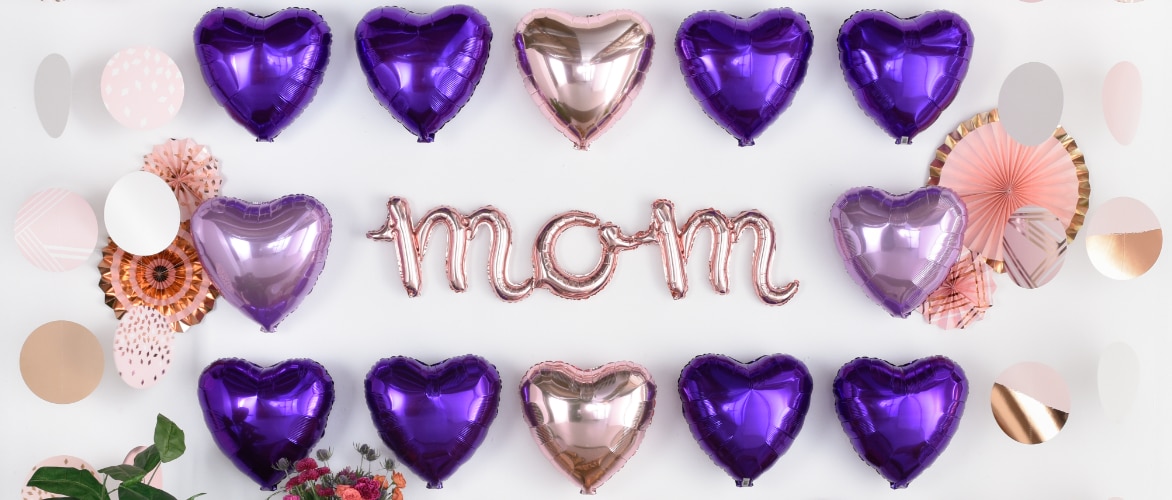 Purple and pink heart-shaped balloons, hanging decor and pink balloons that read "mom". 