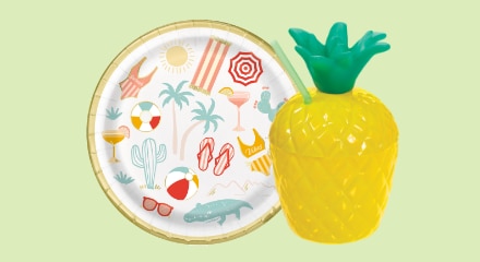 A paper plate with a beach-themed pattern and a pineapple-shaped cup with straw.