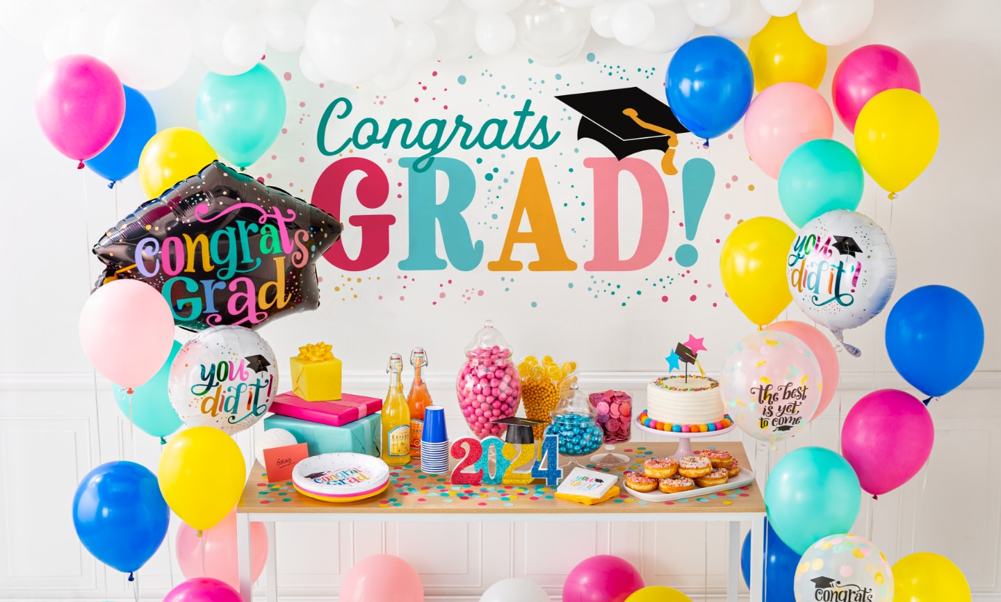 A table set with sweet treats surrounded by celebratory graduation themed wall decorations and balloons.