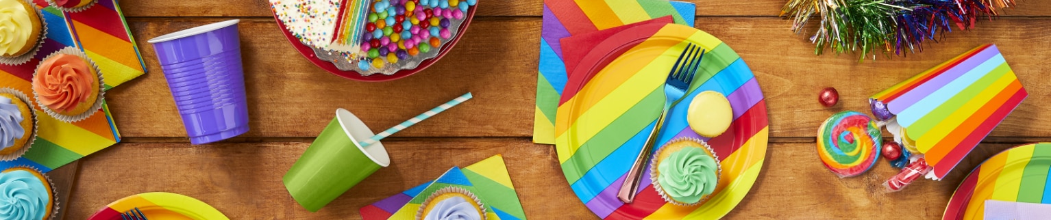 An overhead shot of various rainbow-themed tableware, cupcakes, cookies, candy and a cake.