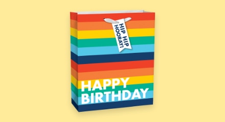 A rainbow-patterned gift bag that reads 'HAPPY BIRTHDAY'.