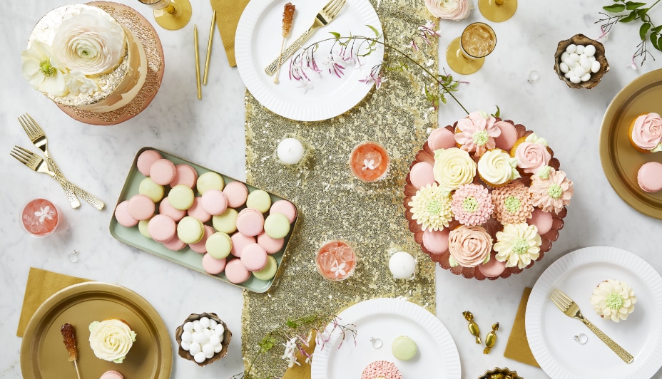 A dessert table styled with white, pink and gold decor, plates, cookies and cupcakes.