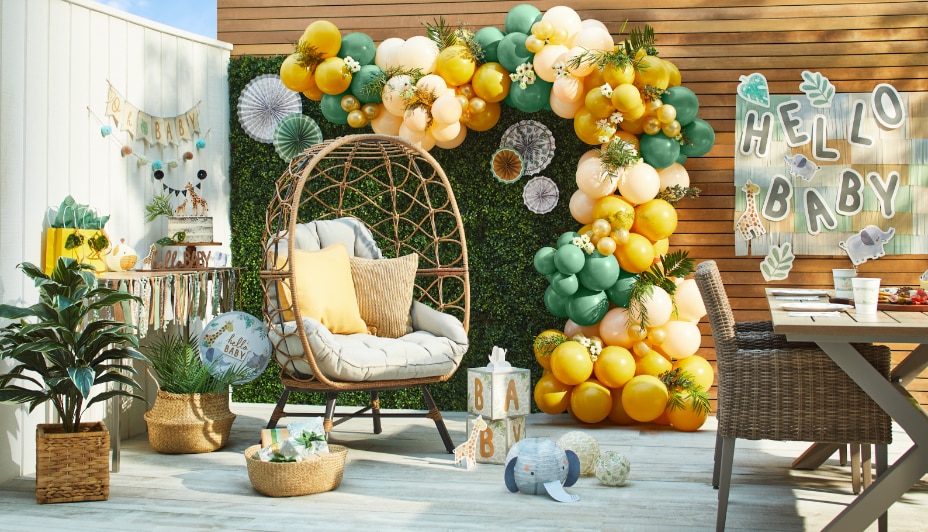 A patio decorated with a yellow and green balloon arch, a “hello baby” banner and various jungle-themed décor.