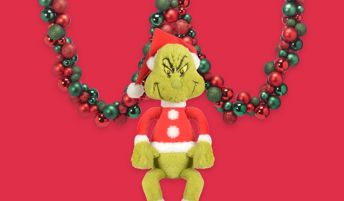 Le Grincheux habillé en Père Noël devant une guirlande festive rouge et verte.