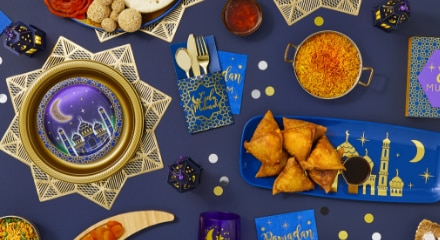 A table decorated in gold, blue and purple tableware with gold cutlery amongst a feast laid out for Ramadan & Eid.