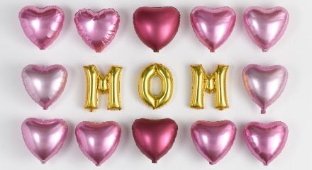 Gold helium-filled letter balloons that spell mom surrounded by red and pink foil heart balloons.