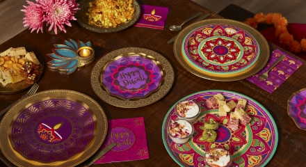 A table decorated for Diwali with multi-coloured gold, purple and magenta plates and napkins next to a teal tea light and pink flowers.