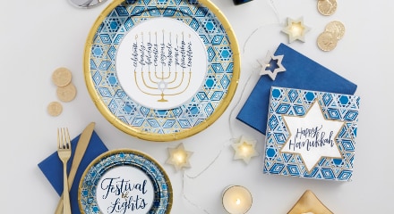 A table decorated for Hanukkah with blue, white, gold and silver plates, blye and gold napkins, gold cutlery, silver stars and gold coins.