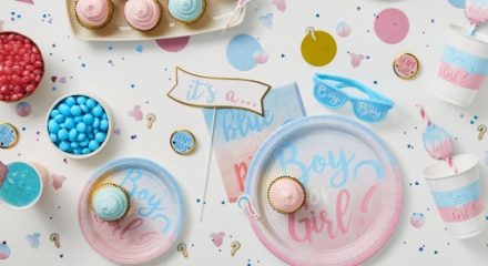 A white table decorated with sweet treats, blue and pink decorations, plates, napkins and cups that say 'Boy or Girl?' for a Gender Reveal party.