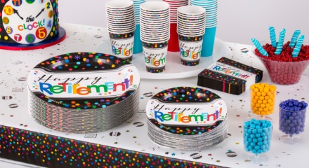 A table decorated for a retirement party with candy, a top hat with a countdown clock on it, black and multi-coloured dot napkins, plates and cups that say 'Happy Retirement' printed on the front.