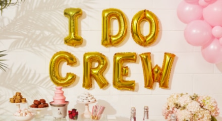 A white room with a table decorated for a bachelorette party, pink balloons and gold letter balloons that say 'I Do Crew'.