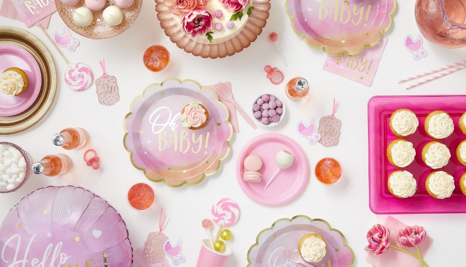 Une table blanche, rose et violette décorée pour une fête prénatale avec des petits gâteaux, des bonbons et de la vaisselle qui dit « Oh Baby ».