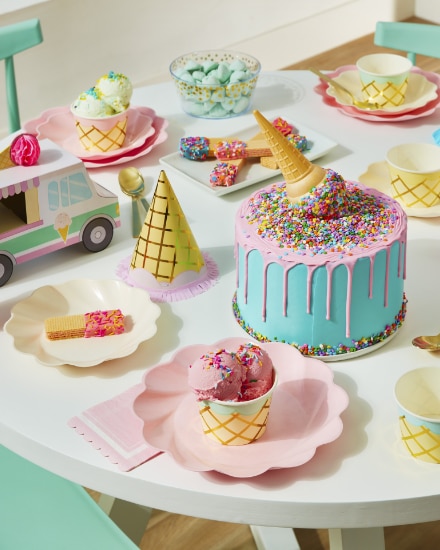 Table avec des tasses à crème glacée à thématique de cornets, des chapeaux de fête et un gâteau.