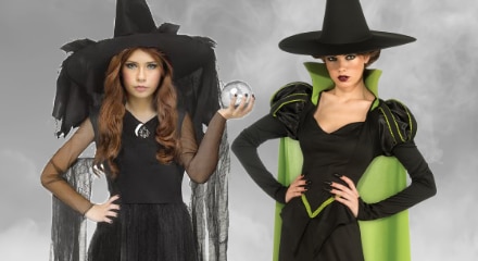 Two people dressed as witches: one in a black dress with a crystal ball, and the other in a green and black outfit with a cape.