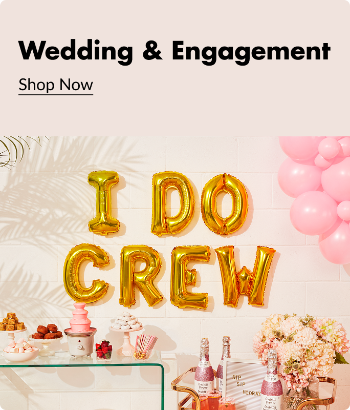 Gold letter balloons that spell out 'I Do Crew' sitting against a wall next to a pink balloon bouquet and above a table decorated with snacks, drinks and flowers. 